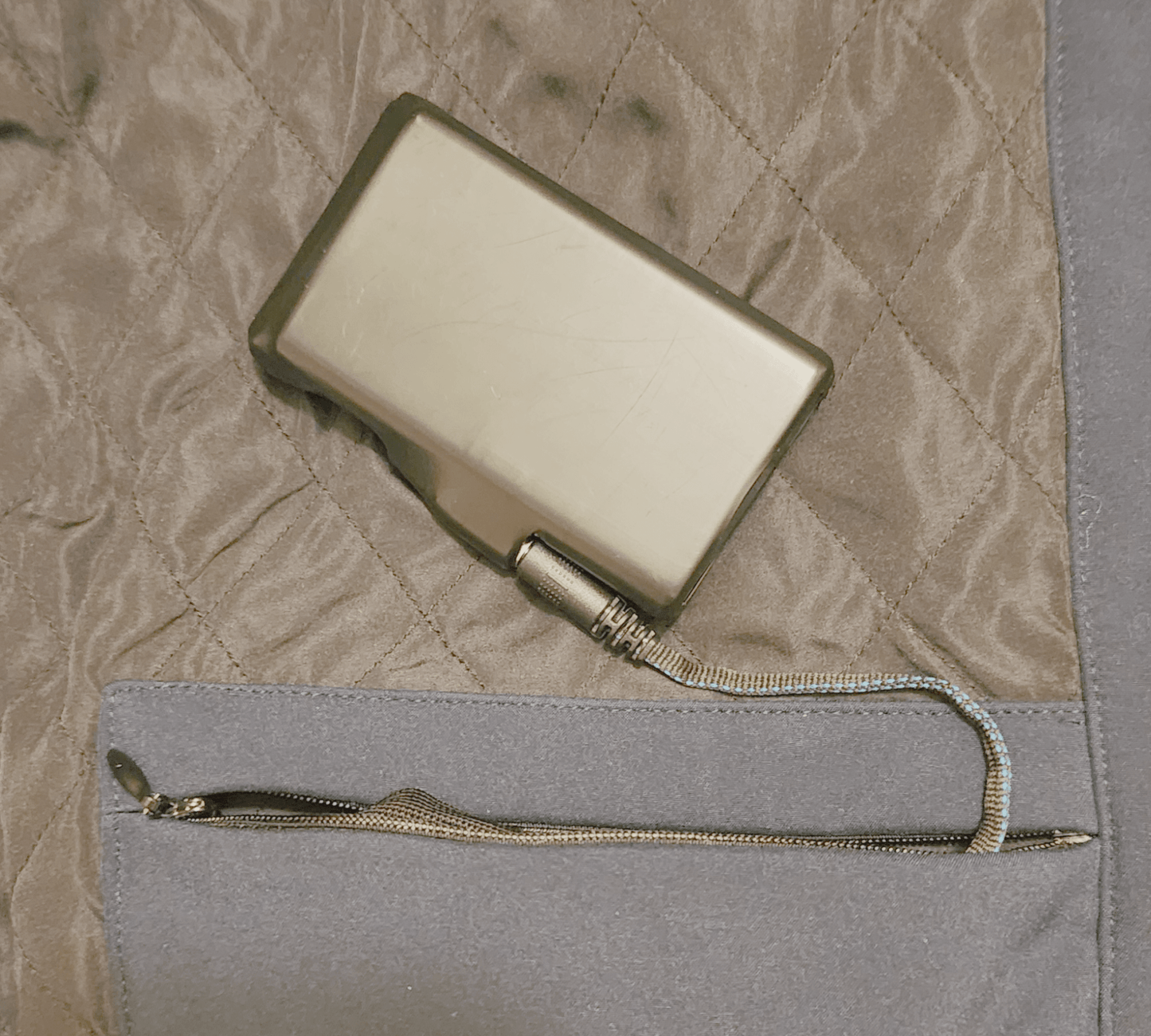 Image showing a battery connected to the Jacket's heating system via the connector in the interior jacket battery storage pocket.